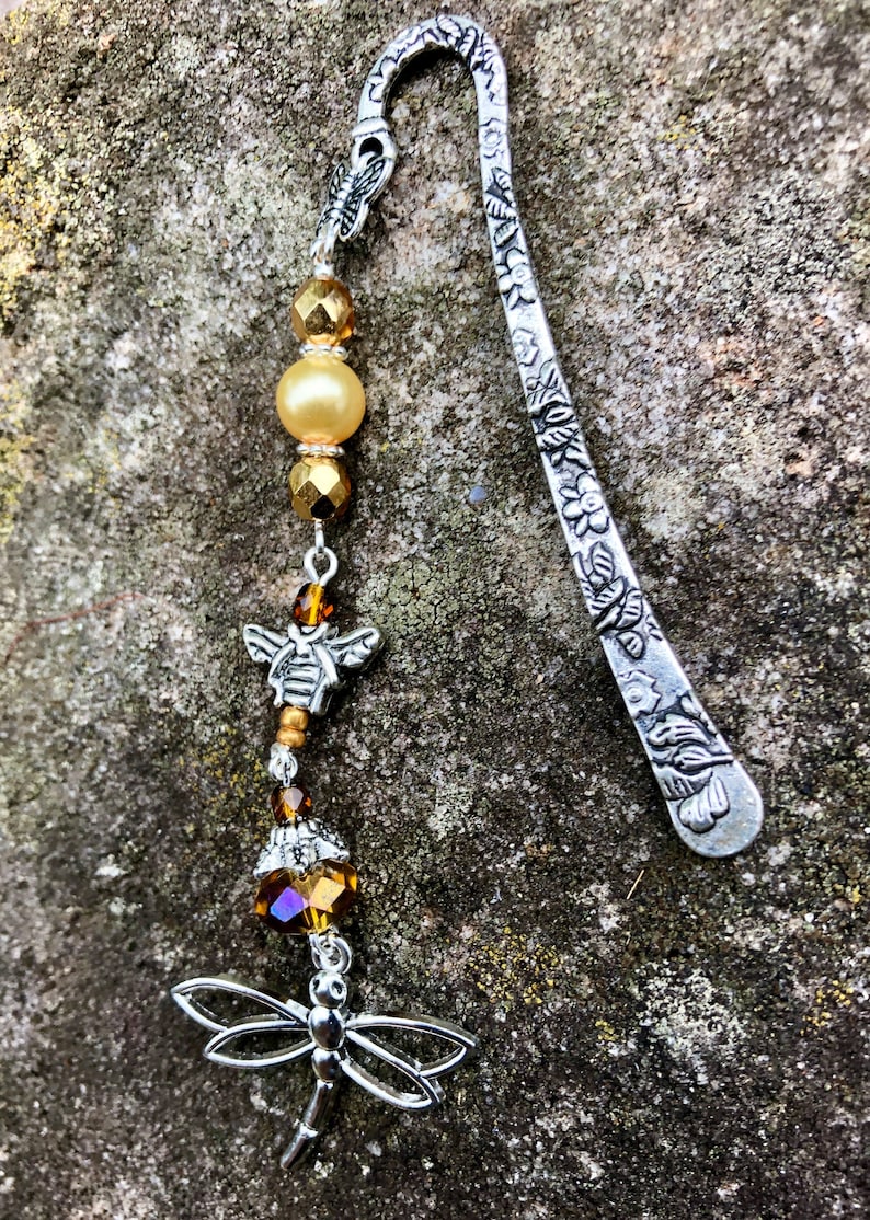 May include: Silver bookmark with a floral design and a dangling charm featuring a bee, beads, and a dragonfly.