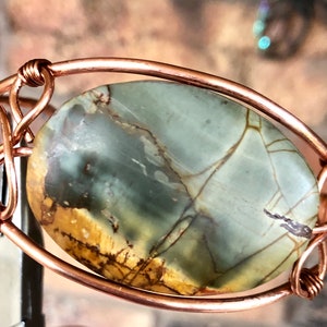K&ouml;nnte beinhalten: Ein Armband aus Kupferdraht mit einem gr&uuml;n-braunen Achat-Stein. Der Stein ist oval geformt und hat ein nat&uuml;rliches Muster.