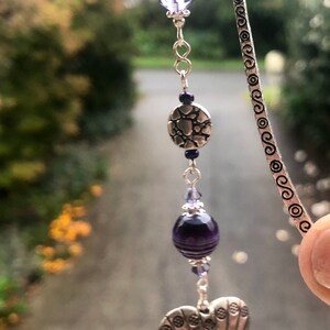 May include: A silver bookmark with a heart-shaped charm, a round charm with a textured design, and purple glass beads.