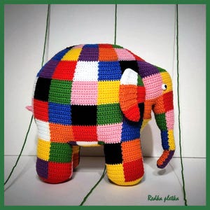 May include: A crocheted elephant toy featuring a vibrant patchwork design of multicolored squares in red, blue, yellow, green, black, white, and pink. The elephant has a trunk, a single visible eye, and the text Redka pletka printed in green.