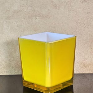 May include: A square yellow glass candle holder with a white interior.