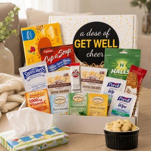 Könnte beinhalten: Eine weiße Geschenkbox mit der Aufschrift A dose of GET WELL cheer, die verschiedene Artikel enthält, darunter Lipton Cup-a-Soup, Swiss Miss Kakao, Westminster Bakers Austerncracker, Emergen-C, Twinings Teebeutel, Halls-Bonbons und Purell-Tücher.