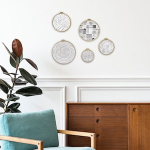 May include: Five black and white patterned embroidery hoops hanging on a white wall. The hoops are different sizes and have different patterns. The hoops are hanging in a staggered pattern.