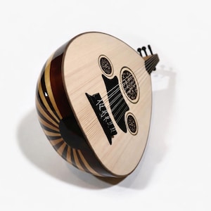May include: An oud, a Middle Eastern stringed instrument, with a light wood face and dark accents. The instrument has a rounded body and a short neck. The back features a sunburst design. The strings are visible. The oud is made of wood.