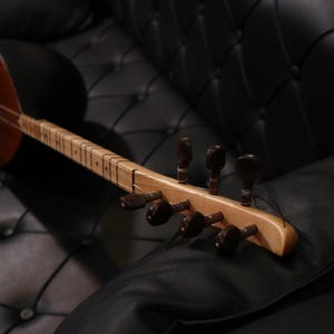 Könnte beinhalten: Ein hölzernes Saiteninstrument mit braunem Korpus und hellem Holz Hals. Das Instrument hat eine Reihe von Stimmwirbeln am Hals.