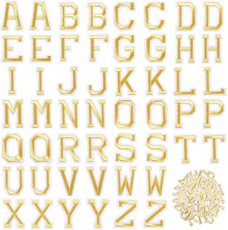 Op de afbeelding: Gouden strijkletters van het alfabet, van A tot Z, in een klassieke blokletter-stijl. De letters zijn ongeveer 2,5 cm hoog en hebben een witte omtrek. In de rechterbenedenhoek van de afbeelding bevindt zich een kleine stapel extra letters.