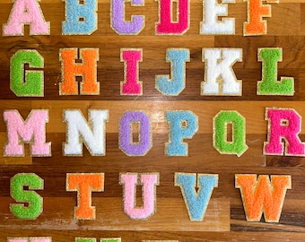May include: A set of 26 colorful felt letters with gold glitter trim. The letters are arranged in alphabetical order on a wooden surface.