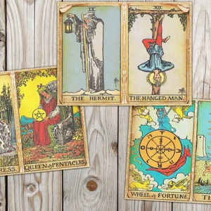 May include: A set of ten tarot cards with colorful illustrations and gold trim. The cards include The Empress, Queen of Pentacles, The Hermit, The Hanged Man, Wheel of Fortune, and The Moon.