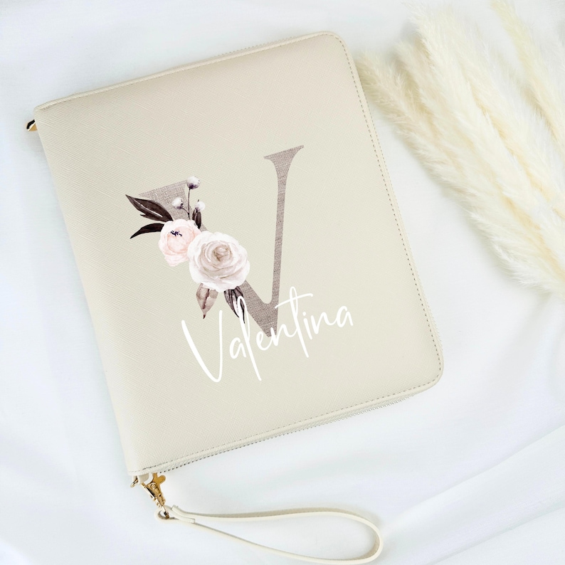 May include: A beige zippered pouch with a floral design and the letter "V" in a brown font. The name "Valentina" is written in white script below the letter.