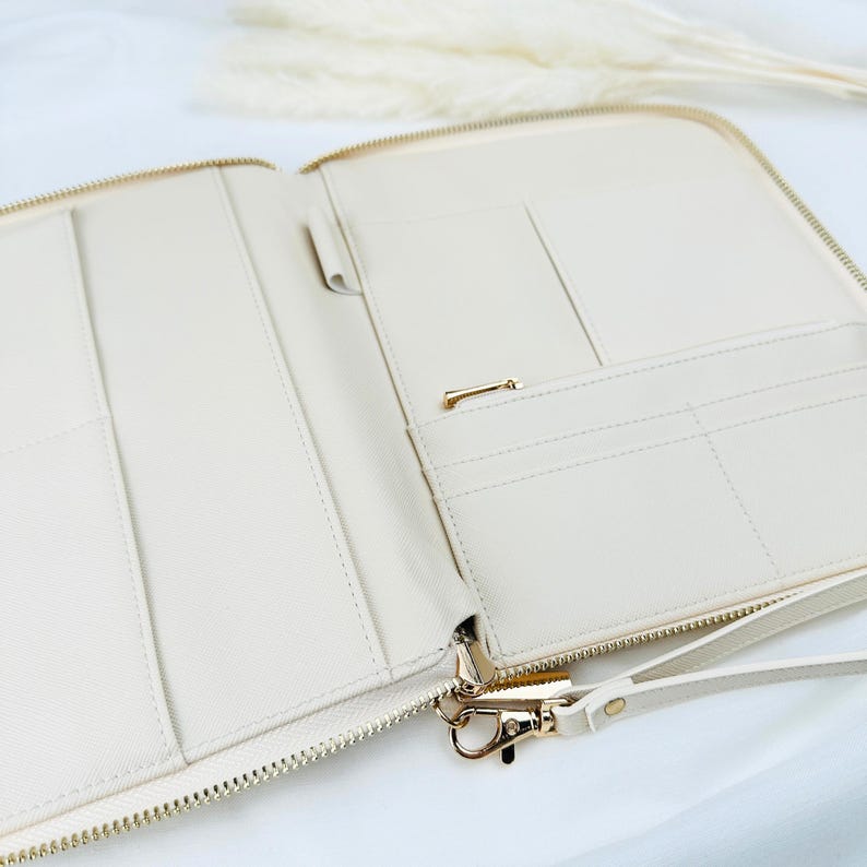 May include: A cream-coloured zippered pouch with multiple pockets and a gold zipper. The pouch has a gold hook and a cream-coloured strap.