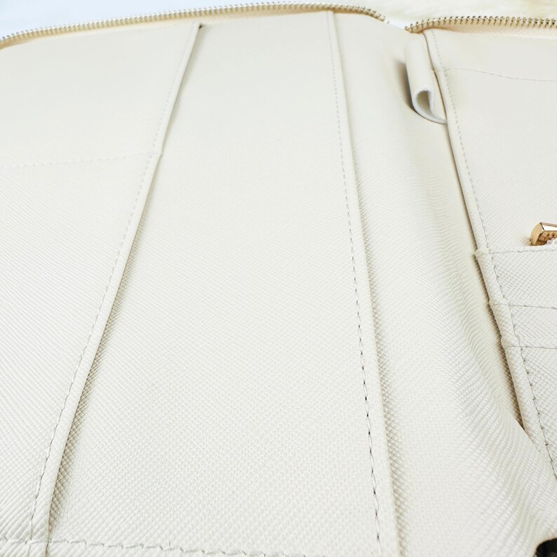 May include: A white leather zipped folder with multiple pockets and compartments. The folder is open and the interior is visible.