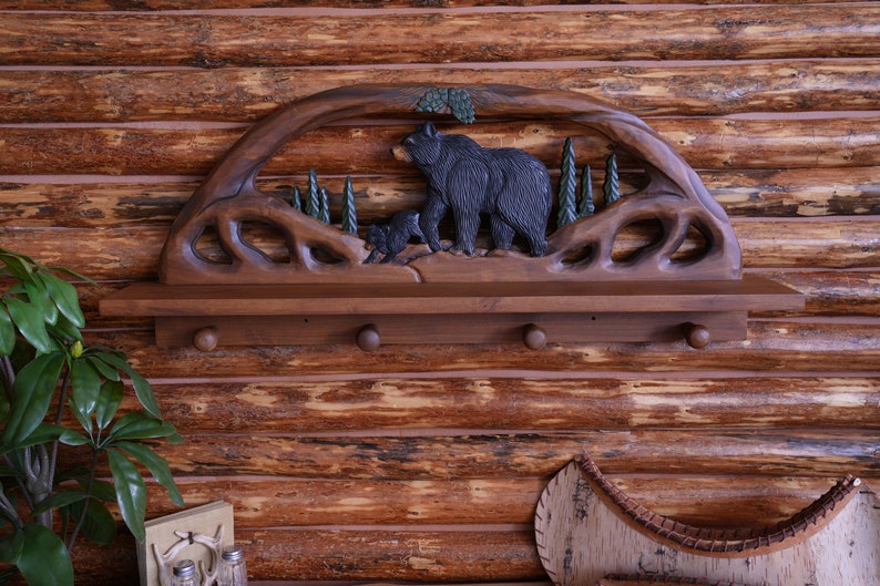 Puede incluir: Una estanter&iacute;a de madera con un dise&ntilde;o tallado de un oso y un cachorro. La estanter&iacute;a tiene cuatro ganchos y est&aacute; te&ntilde;ida de un color marr&oacute;n oscuro.