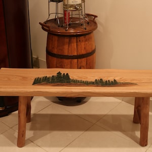 May include: A wooden bench with a natural wood finish and a green tree design carved into the top. The bench has two legs on each side and is made of solid wood.
