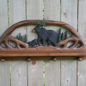 Puede incluir: Una estanter&iacute;a de madera con un dise&ntilde;o tallado de un oso y un cachorro. La estanter&iacute;a tiene un tinte marr&oacute;n y cuatro ganchos en la parte inferior.