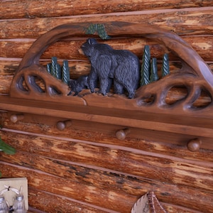 Puede incluir: Una estanter&iacute;a de madera con un dise&ntilde;o tallado de oso y pino. La estanter&iacute;a tiene tres ganchos y est&aacute; te&ntilde;ida de un color marr&oacute;n oscuro.