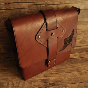 May include: A brown leather messenger bag with a flap closure and a decorative design. The bag features a buckle closure and a strap. The bag is made of leather and has a vintage look.