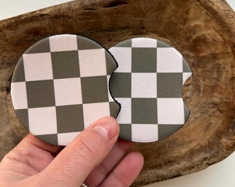 May include: Two round, black-rimmed, checkered drink coasters. The coasters are made of a soft, absorbent material and feature a white and olive green checkered pattern.