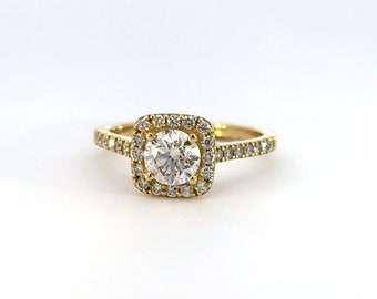 Könnte beinhalten: Ein goldener Verlobungsring mit einem quadratischen Halo-Setting und einem runden Diamanten in der Mitte. Die Ringschiene ist ebenfalls mit kleinen Diamanten besetzt.