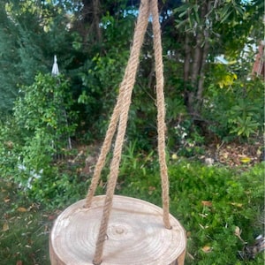 May include: A round wooden slice hanging from a thick rope, perfect for displaying small plants or decorative items.