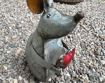 May include: A metal mouse sculpture crafted from weathered gray sheet metal with large, rounded ears and a pointed snout. The mouse features a small, glossy red heart held between its front paws and has simple, dark painted eyes.