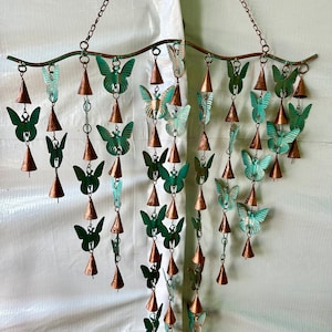 May include: A metal wind chime with multiple tiers of hanging copper bells and green butterfly cutouts. The chime is suspended from a curved metal rod.