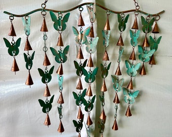 May include: A metal wind chime with multiple tiers of hanging copper bells and green butterfly cutouts. The chime is suspended from a curved metal rod.