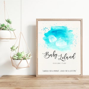 Puede incluir: Una impresión acuarela enmarcada de una imagen de ultrasonido de bebé en tonos azules. La impresión presenta el texto "Baby Leland" y la fecha "Feb 28, 2020 | 15th Week". La cita "Carried for a moment, loved for a lifetime." está impresa debajo de la imagen.