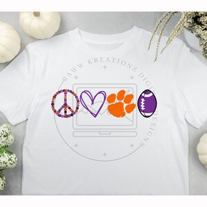 May include: White t-shirt featuring a purple peace sign, a purple heart, an orange paw print, and a purple football within a circle containing the text "RAWW KREATIONZ DIGITAL DESIGNS".