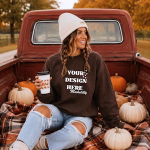 May include: A dark brown crewneck sweatshirt featuring the white text "YOUR DESIGN HERE Mockalilly" with small heart icons, paired with light blue distressed denim jeans and a cream-colored ribbed knit beanie hat.