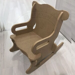 May include: A wooden rocking chair for children, made of unfinished plywood. The chair has a high back and armrests, and the rocking base is visible.