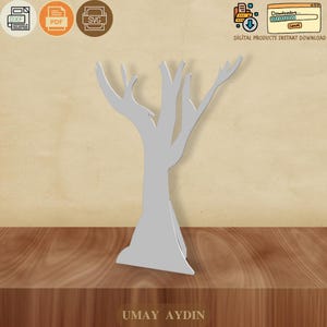 Pode incluir: Um recorte de árvore estilizado em cinza claro, com uma base larga e vários galhos. A árvore está posicionada sobre uma superfície de madeira. A imagem inclui ícones para os formatos de arquivo DXF, PDF e SVG, juntamente com o texto "DOWNLOAD INSTANTÂNEO DE PRODUTOS DIGITAIS". O nome "UMAY AYDIN" está na parte inferior.