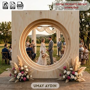 May include: A large, circular wooden wedding arch with a light natural grain finish, featuring a square frame design. The arch is decorated with two floral arrangements of pampas grass, white roses, and pink peonies at the base. Digital product file.