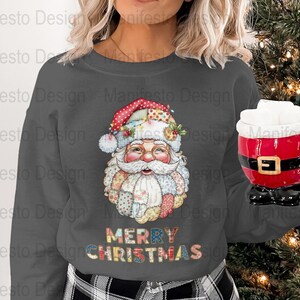 Puede incluir: Sudadera gris oscuro con un diseño de Papá Noel. El diseño de Papá Noel presenta un estilo patchwork con un gorro y barba rojos y blancos. Las palabras "MERRY CHRISTMAS" se muestran en letras coloridas. Se sostiene una taza roja de Papá Noel.