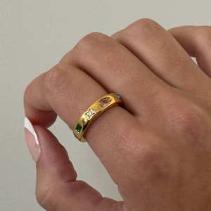 Może przedstawiać: Złoty pierścionek z różowym kamieniem i zielonymi i niebieskimi akcentami.