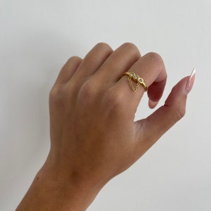Op de afbeelding: Gouden ring met drie kleine heldere stenen en een hangende ketting.