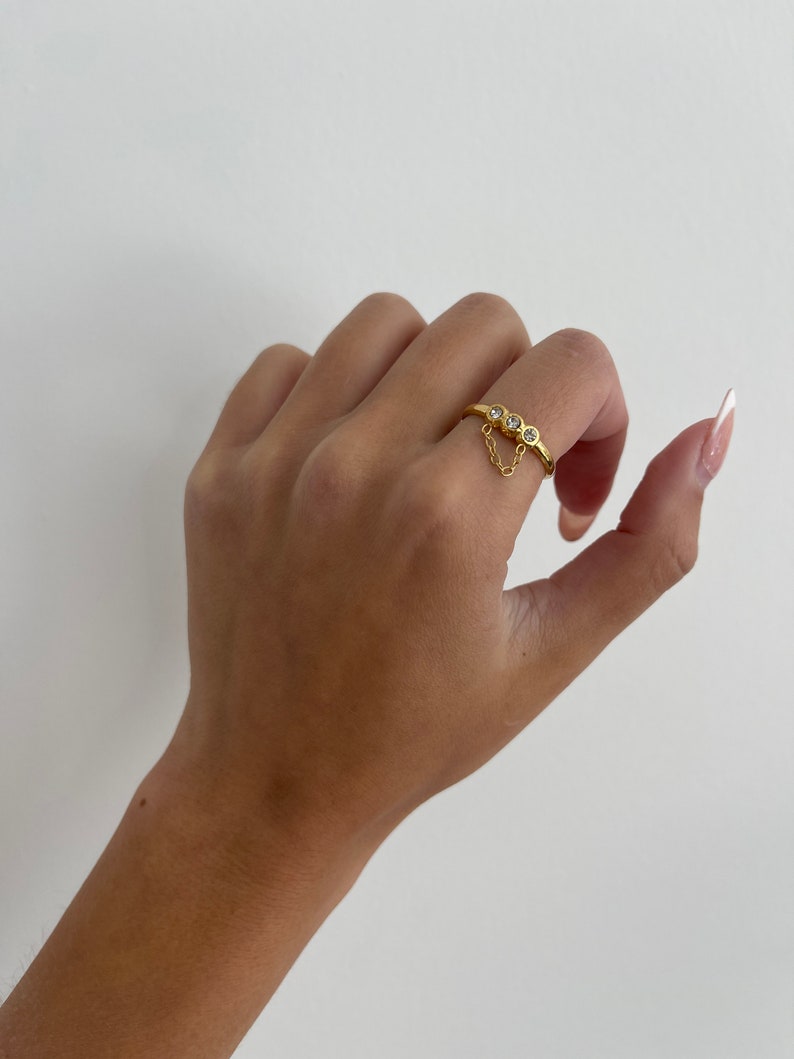 Op de afbeelding: Gouden ring met drie kleine heldere stenen en een hangende ketting.