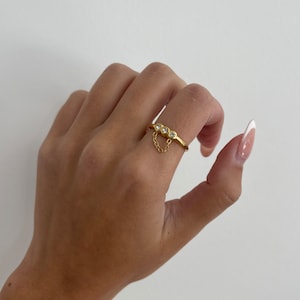 Op de afbeelding: Gouden ring met een hangende ketting en vier heldere stenen.