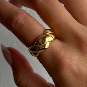 May include: A gold-toned ring with a twisted design. The ring is thick and has a smooth, polished finish.