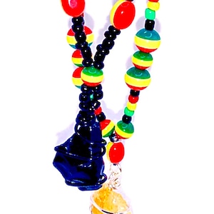 May include: A beaded necklace featuring a combination of red, yellow, green, and black beads. The necklace has a dark blue pendant and a yellow stone pendant wrapped in silver wire. The necklace is displayed against a white background.