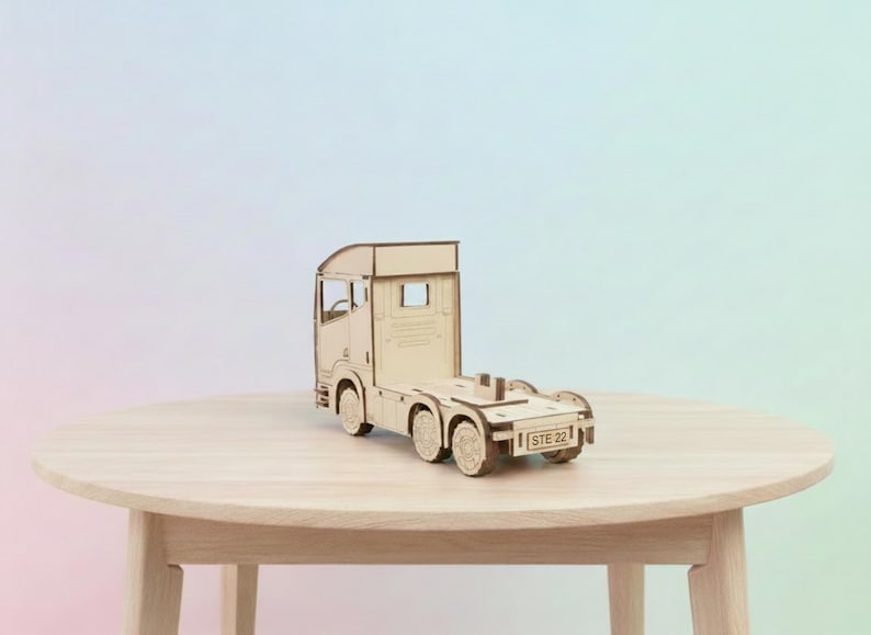 May include: A detailed wooden model of a truck cab and chassis, with visible wheels and design features. The model is made of light-coloured wood and is placed on a round wooden table. The text "STE 22" is visible on the back.