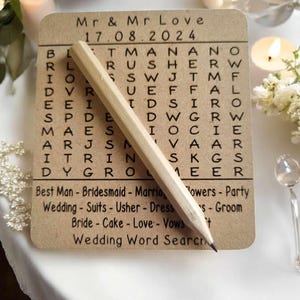 May include: A brown card with a wedding word search puzzle. The puzzle features the words "Mr. & Mr. Love" and "17.08.2024". The words "Best Man", "Bridesmaid", "Marriage", "Flowers", "Party", "Wedding", "Suits", "Usher", "Dress", "Bride", "Cake", "Love", "Vows", and "Groom" are listed below the puzzle.