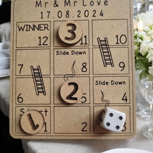 May include: A wooden game board with a brown background and black text. The board is a game of snakes and ladders. The board has a title that says "Mr & Mr Love 17.08.2024". The board has a winner square that says "Winner 12". The board has a dice and wooden tokens with numbers on them.
