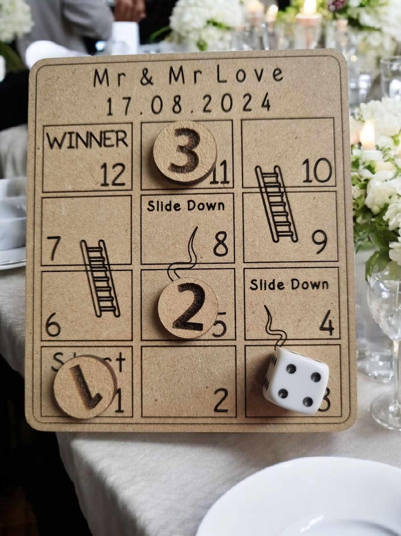May include: A wooden game board with a brown background and black text. The board is a game of snakes and ladders. The board has a title that says "Mr & Mr Love 17.08.2024". The board has a winner square that says "Winner 12". The board has a dice and wooden tokens with numbers on them.