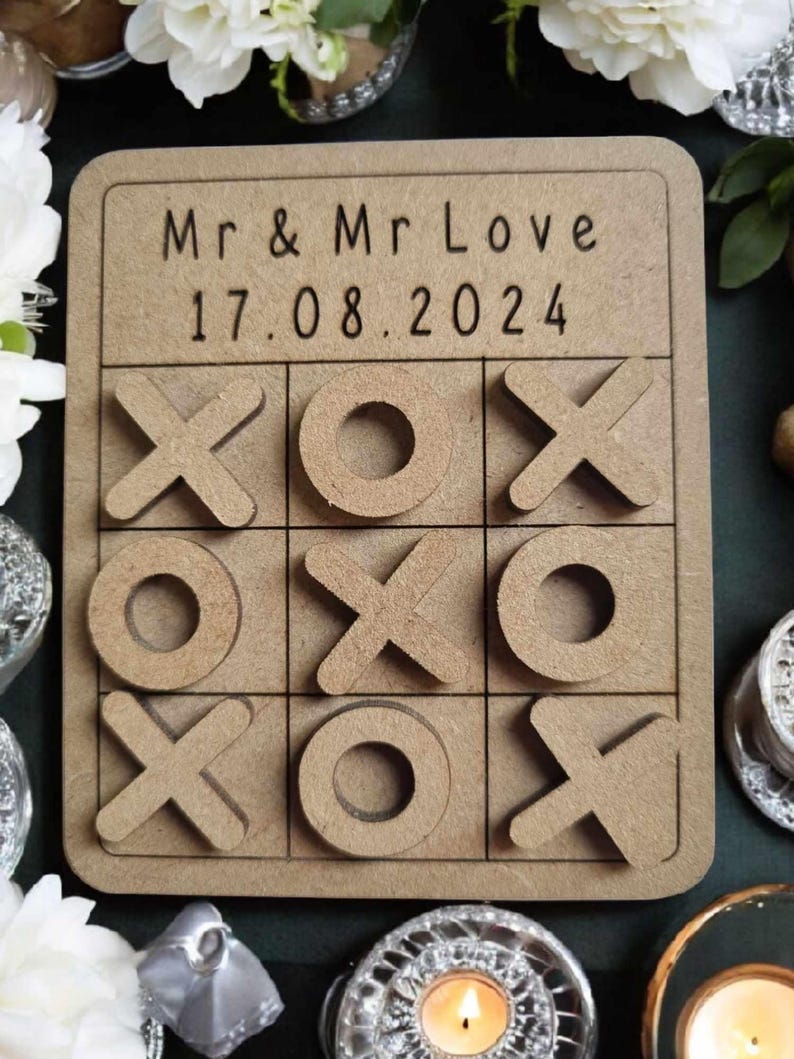 May include: A wooden tic-tac-toe game with the text "Mr & Mr Love 17.08.2024" on the top. The game board is brown and has a white background.