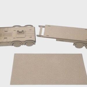 May include: A flat-pack wooden toy truck and trailer. The truck cab and trailer are separate, with a rectangular base piece. The truck has detailed cutouts for windows and other features. The set is made of unfinished wood.