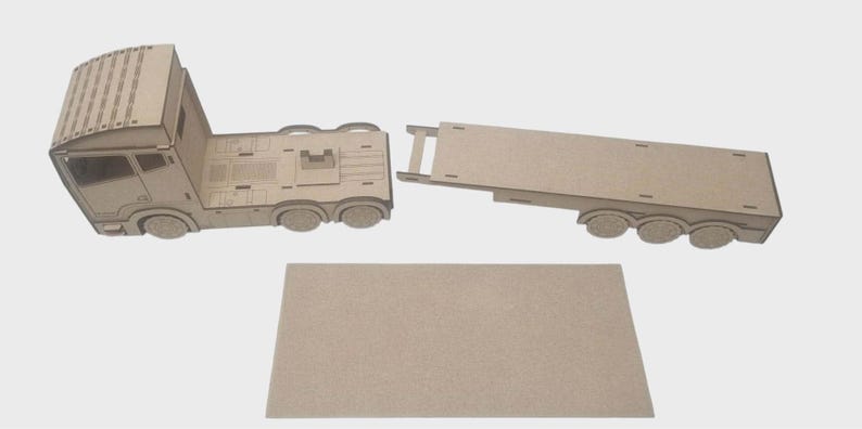May include: A flat-pack wooden toy truck and trailer. The truck cab and trailer are separate, with a rectangular base piece. The truck has detailed cutouts for windows and other features. The set is made of unfinished wood.