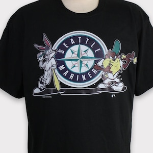 May include: Black t-shirt featuring Bugs Bunny and Taz from Looney Tunes, with a Seattle Mariners logo. The graphic shows the characters in baseball poses, with the team's name and a compass rose design. A vintage style tee.