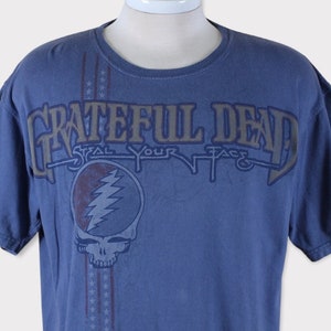 Puede incluir: Una camiseta azul con un estampado descolorido del logotipo de Grateful Dead y el texto "Steal Your Face".
