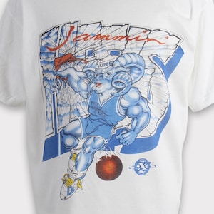 May include: White t-shirt featuring a blue and red graphic of a ram playing basketball. The word "Summit" is printed above the ram. The ram is wearing a blue basketball uniform and holding a basketball.