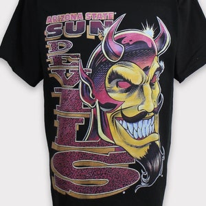 Puede incluir: Camiseta negra con un gráfico de la cabeza de un diablo de dibujos animados con el texto "Arizona State Sun Devils" en dorado y granate.